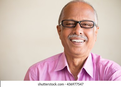 Closeup portrait, smart elderly man in pink shirt with dark eye glasses, specs, sitting down laughing, isolated indoors white chalkboard background