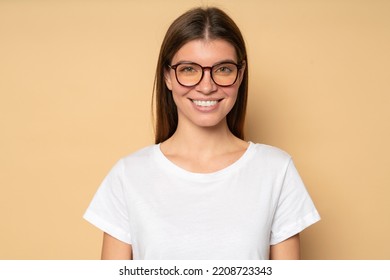 Closeup portrait of smart student girl of 20s in glasses and white mockup t-shirt with copy space for your promo content, looking at camera with candid confident smile on brown studio background
