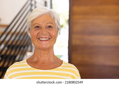 Close-up portrait of smiling biracial senior woman with short hair against door in nursing home. Wood, happy, face, unaltered, support, assisted living and retirement concept. - Powered by Shutterstock