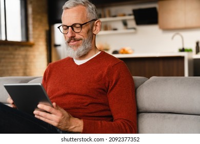 Closeup portrait of a smiling caucasian middle-aged mature man in glasses using digital tablet for e-learning, paying bills online, e-commerce, remote work, social media online at home - Powered by Shutterstock