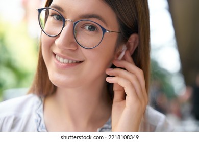 Closeup Portrait Of Smiling Caucasian Woman Wearing Eyeglasses Listening Music Holding Earphones, Looking At Camera, Selective Focus. Wireless Technology Concept 