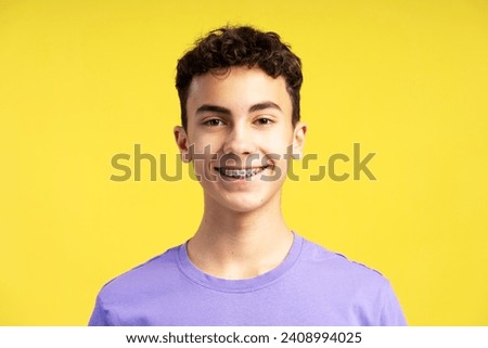 Closeup portrait of smiling confident  boy with dental braces on teeth looking at camera isolated on yellow background. Health care, orthodontic concept 