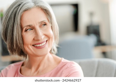 Closeup portrait smiling confident senior woman sitting on comfortable sofa at home. Happy retired female with stylish gray hair, white teeth looking away. Natural beauty, healthy lifestyle concept - Powered by Shutterstock