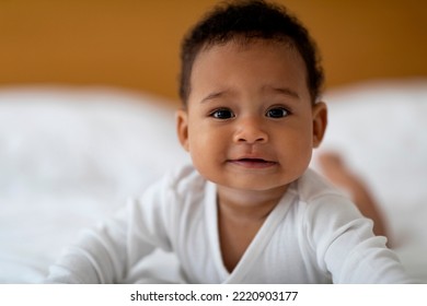 Closeup Portrait Of Smiling Cute Little Black Baby Relaxing On Bed, Adorable African American Infant Boy Or Girl Lying On His Tummy And Looking At Camera While Resting In Bedroom At Home, Copy Space