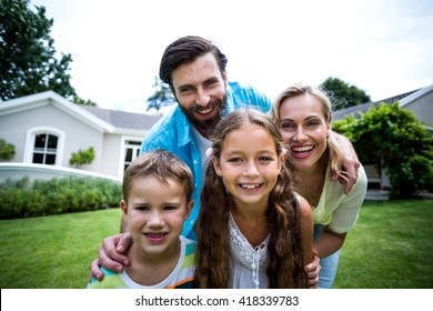 Close-up Portrait Of Smiling Family Standing Outside House In Yard