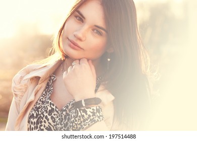 Close-up portrait of smiling girl in sunlight. She stands alone in the park. Photo in warm orange colors