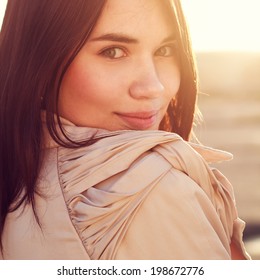 Close-up portrait of smiling girl in sunlight. She stands alone in the park. Photo in warm orange colors