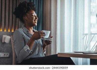 Close-up portrait of a smiling happy charming beautiful dreamer with black curly hair of a mature woman, drinking fresh morning coffee and sitting at a table in a hotel. - Powered by Shutterstock