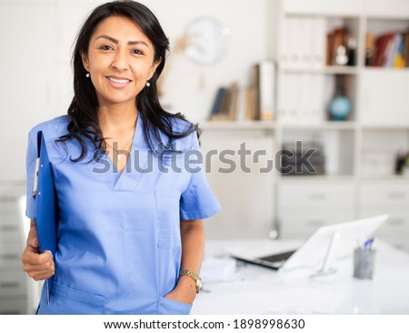 Closeup portrait of smiling hispanic woman health worker wearing blue uniform standing in medical office