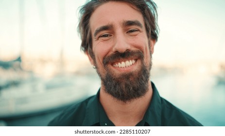 Close-up portrait of a smiling man with a beard on the embankment, on a yacht background. Frontal closeup of happy young hipster male looking at camera - Powered by Shutterstock