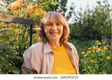 A close-up portrait of a smiling mature woman in casual clothes. A happy pensioner in the garden. A middle-aged woman outdoors. A sunny day. Green trees and flowers. - Powered by Shutterstock