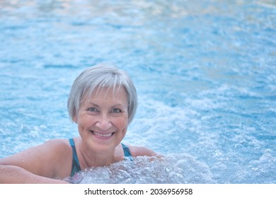 Close-up portrait of smiling senior woman with gray hair looking at camera in outdoor thermal pool with hydromassage. Active ageing concept.