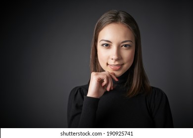 Closeup Portrait Of Smiling Teen Female In Black Pullover With Hand On Chin, Over Dark Studio Background