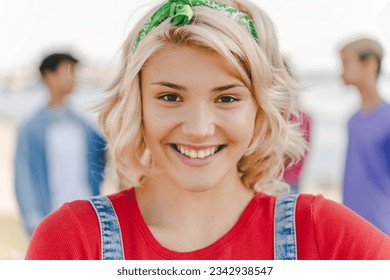 Closeup portrait of smiling идщтву teenage girl wearing red t shirt looking at camera on the street with friends on background. Positive lifestyle, summer concept  - Powered by Shutterstock