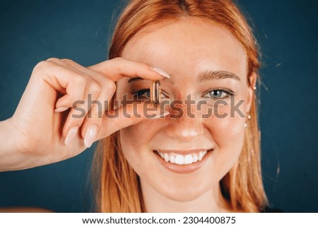 Close-up portrait of smiling woman covering her eye, looking through Omega 3 fish oil capsule. Beautiful girl - healthcare and medical concept