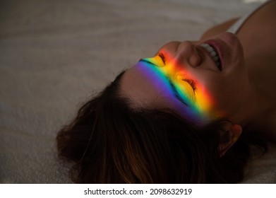 Close-up Portrait Of Smiling Woman With Ray Of Rainbow Light On Her Face. 