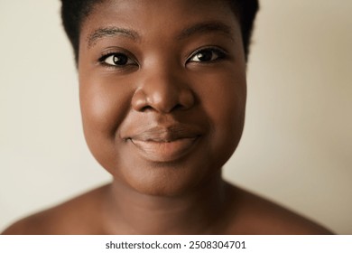 Close-up portrait of a smiling young African woman with bare shoulders and a perfect complexion posing against a light background - Powered by Shutterstock