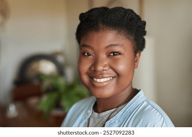 Close-up Portrait of a smiling young African woman standing in the comfortable living room of her home - Powered by Shutterstock