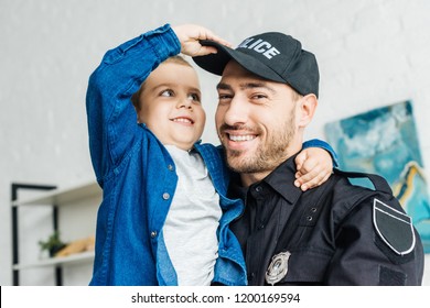 портрет улыбающегося молодого отца в полицейской форме, несущего своего маленького сына и смотрящего в камеру