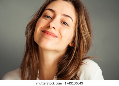 Close-up portrait of a smiling young girl in a white shirt on a gray background. Hands near the face. without retouching and makeup.