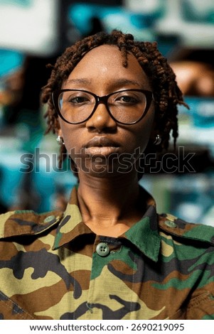 Closeup portrait of soldier in front of command center screens used for surveillance and threat monitoring. African american officer oversees mission control with displays showing intelligence feeds