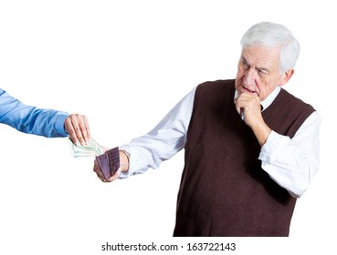 Closeup portrait of someone taking dollar bills currency out of brown wallet from old senior mature elderly business man grandfather with brown sweater.  Guy is sad to be losing his hard-earned income