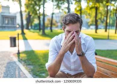 Closeup portrait, stressed young business man, hands on head with bad headache, isolated background of trees outside. Negative human emotion facial expression feelings.