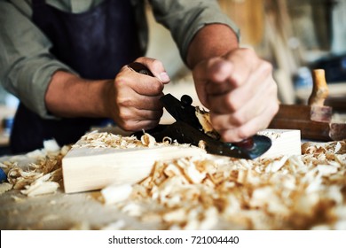 Closeup portrait of strong male hands shaving piece of wood with plane tool in carpenters workshop making furniture