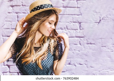 Close-up Portrait Of Stunning Blonde Girl With Hair Waving Posing With Eyes Closed And Cute Smile. Aorable Young Woman In Straw Hat Enjoying Summer Wind While Spending Time Outside.