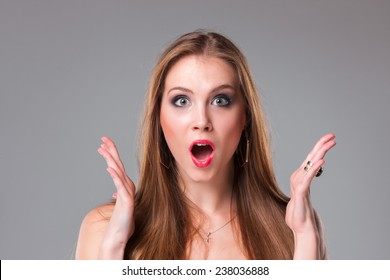 Close-up portrait of surprised beautiful girl holding her head in amazement and open-mouthed. Over gray background.