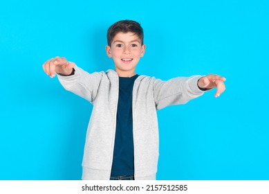 Close-up portrait of surprised caucasian kid boy wearing grey hoodie over blue background pointing with two fingers to the camera saying: I choose you!, looking up with open mouth. - Shutterstock ID 2157512585