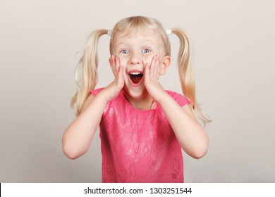 Closeup Portrait Of Surprised White Blonde Caucasian Preschool Girl Making Faces In Front Of Camera. Child Smiling Laughing Posing In Studio On Plain Light Background. Kid Expressing Emotions