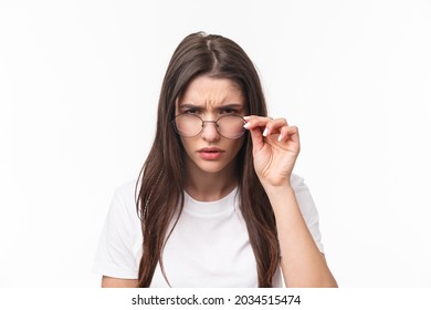 Close-up portrait of suspicious young serious-looking woman, look from under glasses, squinting at person with judgemental disbelief stare, standing white background, have doubts