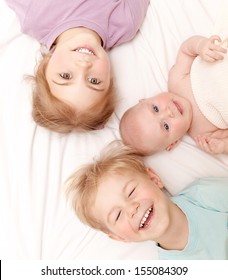 Closeup Portrait Of Three Cheerful Kids Lying Down At Home, Newborn Baby With Brother And Sister, Happy Family, Love And Friendship Concept