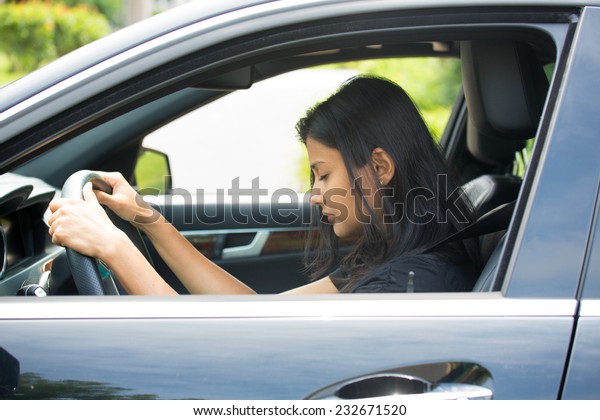 Closeup portrait tired young attractive woman\
with short attention span, driving her car after long hours trip,\
trying to stay awake at wheel, isolated outside background. Sleep\
deprivation