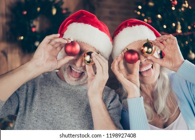 Close-up portrait of two cheerful positive playful nice grey-haired people married spouses grandma grandpa holding round glossy shiny toys covering closing eyes fooling good mood indoors opened mouth
