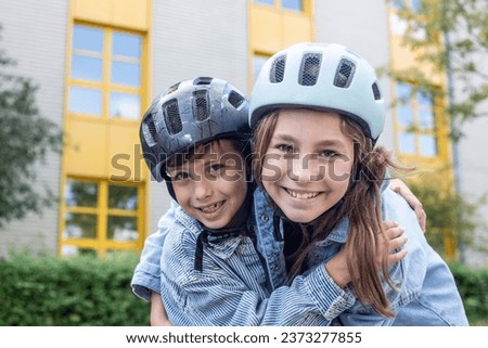 Close-up portrait of two children, boy and girl, hugging, looking at the camera, smiling in helmets, ready to go roller skating or cycling in their free time from lessons in the school yard on break.