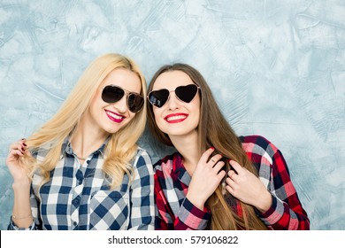 Close-up portrait of two female friends in checkered shirts, jeans and sunglasses on the blue painted wall background