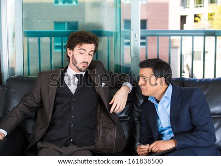 Closeup portrait of two guys in business suits sitting on black couch. One is crying about life problems and other probably caused the trouble or is indifferent. Human emotions and communication  