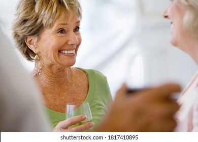 Close-up Portrait Of Two Senior Women Talking At Social Gathering Holding Wine Glasses And Laughing With Differential Focus.