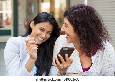 Closeup portrait two surprised girls looking at cell phone, discussing latest gossip news, sharing intimate moments, shopping, laughing at what they see, isolated outdoors background
