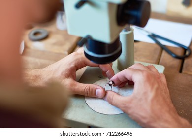 Closeup portrait of unrecognizable jeweler inspecting  ring using microscope on workshop table