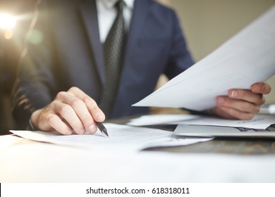 Closeup portrait of unrecognizable successful businessman wearing black formal suit reading documents at desk with laptop, busy with paperwork