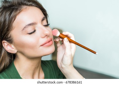 Closeup portrait of a woman applying dry cosmetic tonal foundation on the face using makeup brush. Makeup detail.