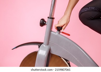 Closeup Portrait Of Woman Hand Fixing Exercise Bike, Doing Sports Workout, Setting An Exercising Machine. Indoor Studio Shot Isolated On Pink Background.