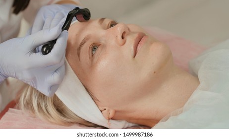Close-up portrait of woman having beauty skin treatment. Therapist preparing skin with derma roller.