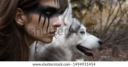 Close-up portrait of a woman hunter with war paint on her cheeks against the backdrop of a wolf face