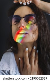 Closeup Portrait Of Woman In Trendy Glasses With Ray Of Rainbow Light On Her Face. Rainbow Optical Flare From The Window Projected On Her Face. Art Beauty Portrait. Girl With Rainbow Shining Face