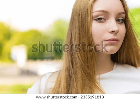 Close-up portrait of a young and attractive Caucasian blonde girl in casual clothes in a green park on a sunny day. Lifestyle concept.