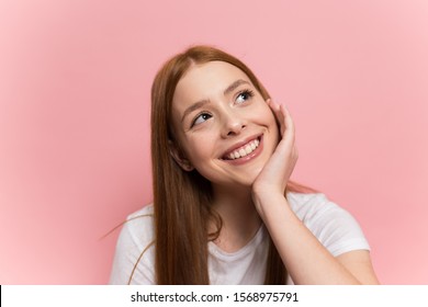 Closeup portrait of a young attractive redhead girl with freckles thinking about something good looking up over orange background - Shutterstock ID 1568975791
